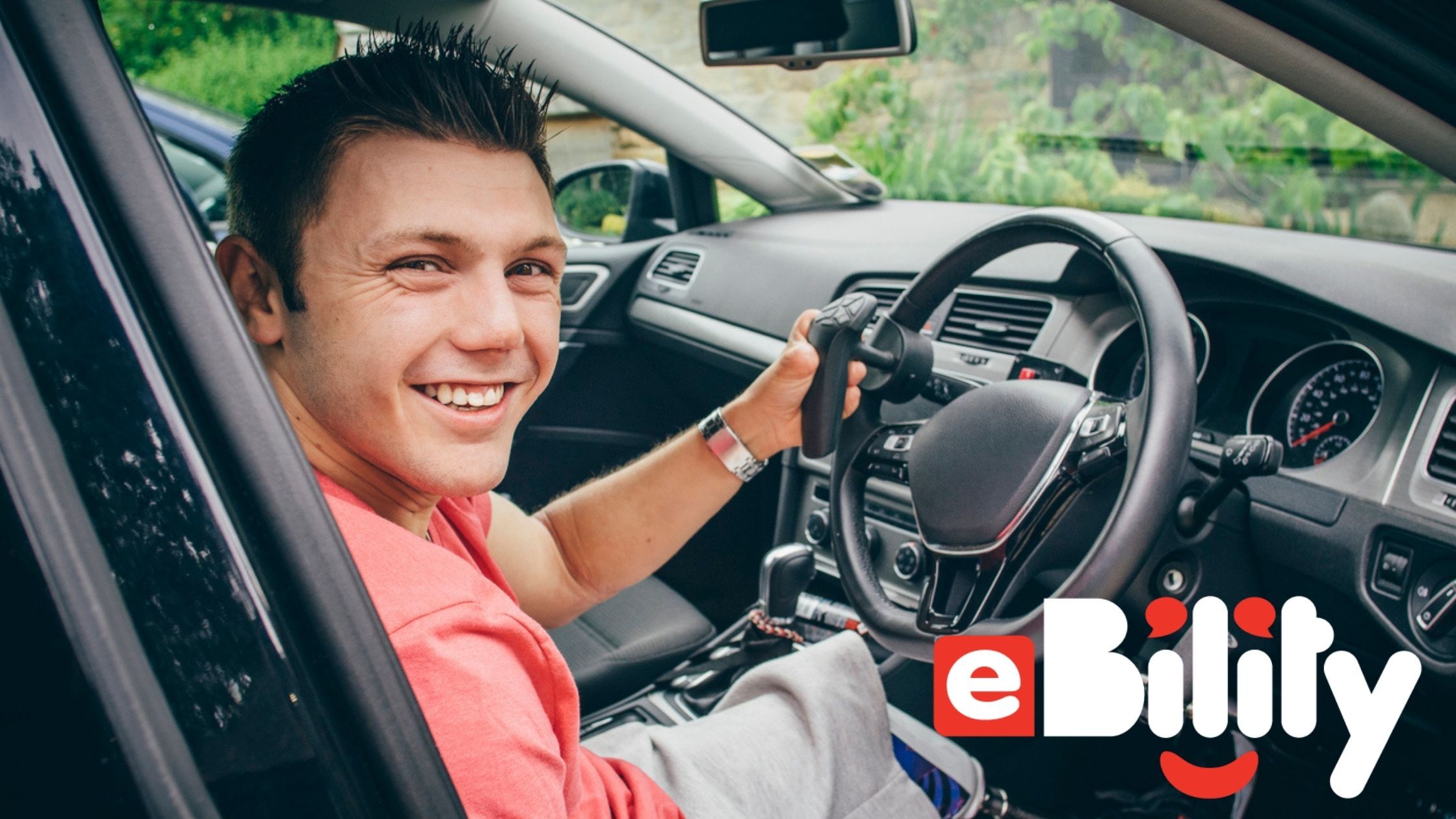 Man sitting in modified vehicle with hand controls on the steering wheel.