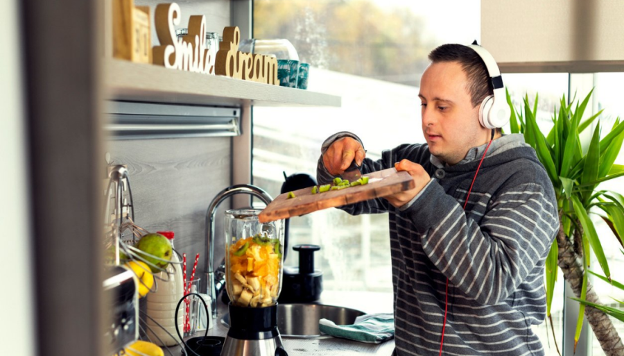 Image of man wearing headphones scraping food off a chopping board into an electric blender.